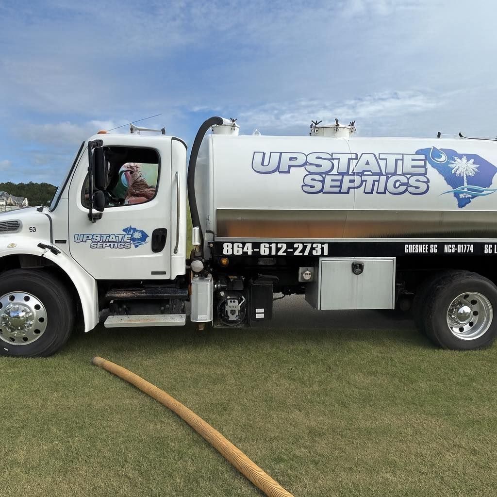 A white Upstate Septics truck parked on grass, featuring a large tank, phone number, and South Carolina graphic.