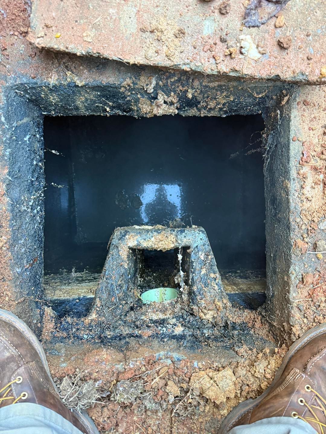 An open, dark rectangular utility or drainage box in the ground, with a small pipe opening visible inside.