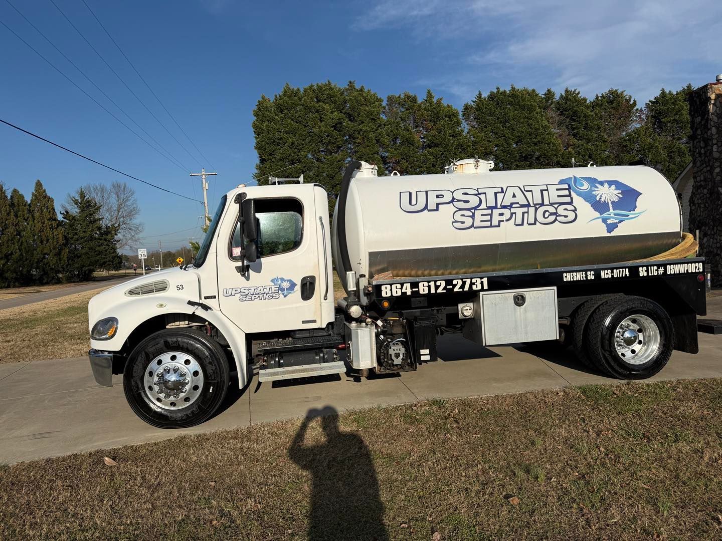 A white Upstate Septics vacuum truck parked on a concrete driveway against a clear blue sky.