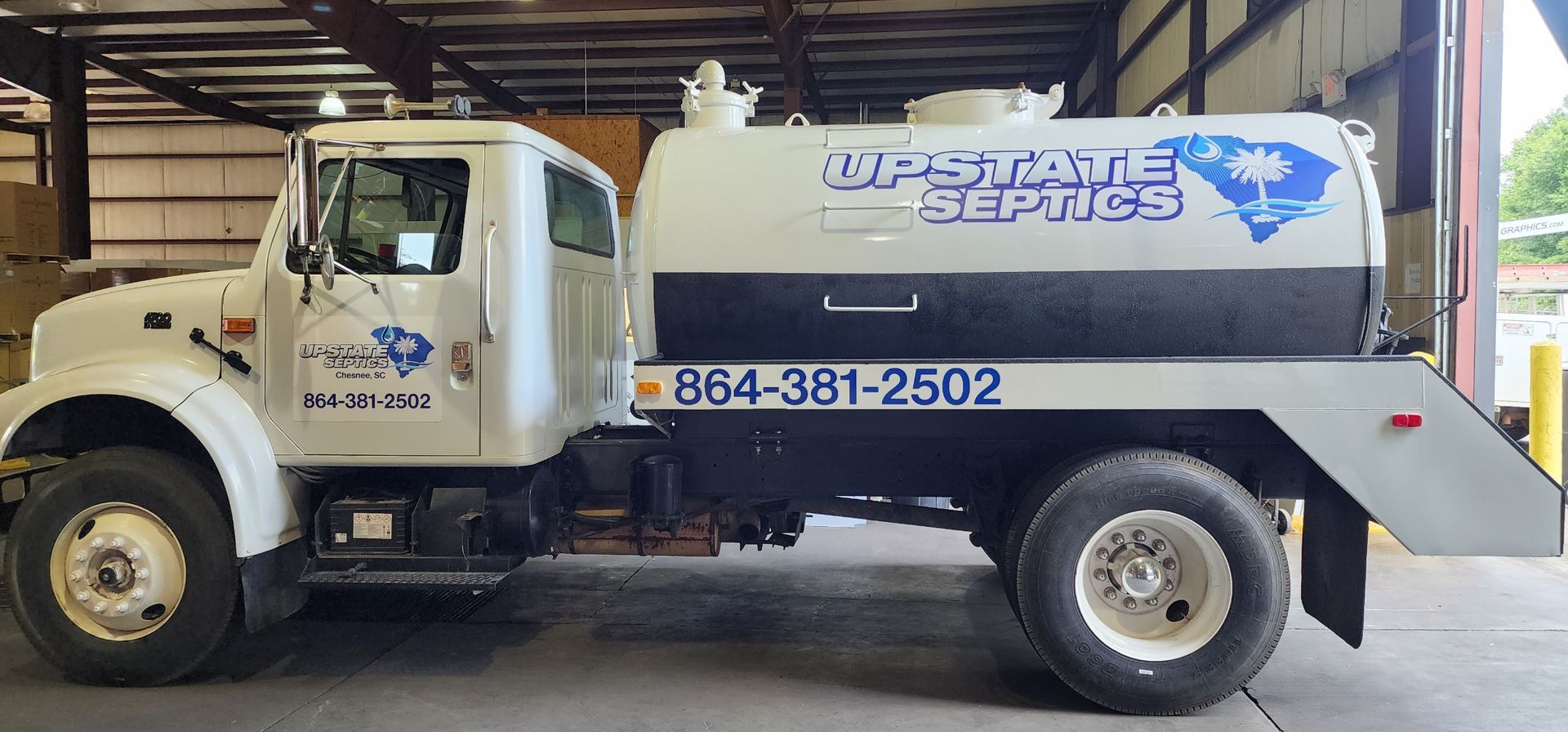 A white and black septic tank truck parked indoors with the text 