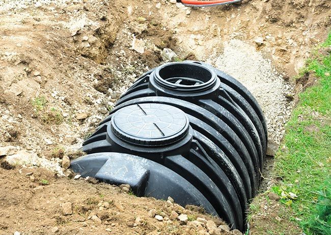 A black plastic septic tank partially buried in a dirt excavation trench.