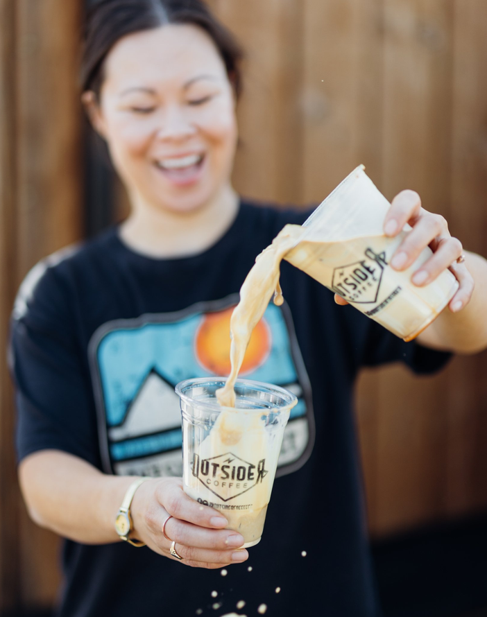 Person pouring a flaming drink from a bottle into a clear glass outdoors