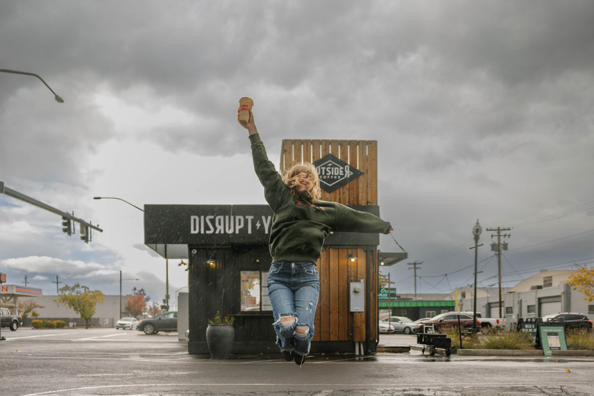 Person jumping in front of a Biscuit on Main sign on a rainy city street
