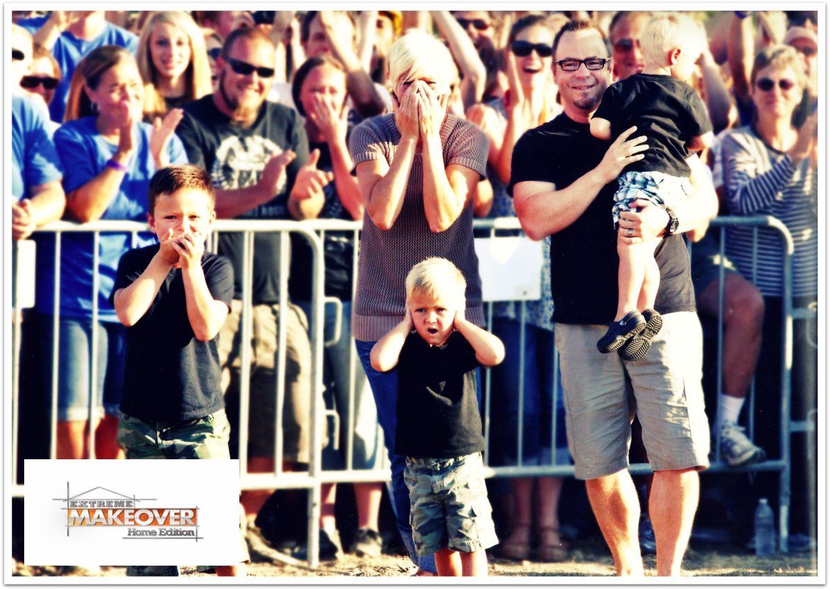Crowd behind a metal barrier watches and cheers while a man holds a child in front.