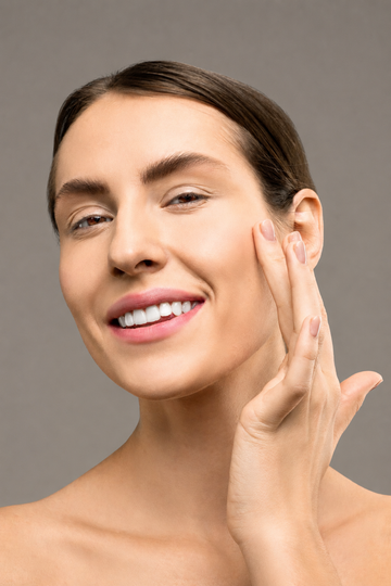 Smiling woman touching her cheek against a plain gray background