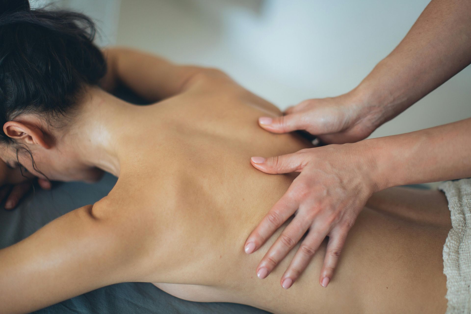 Massage therapist’s hands pressing a client’s bare back on a treatment table