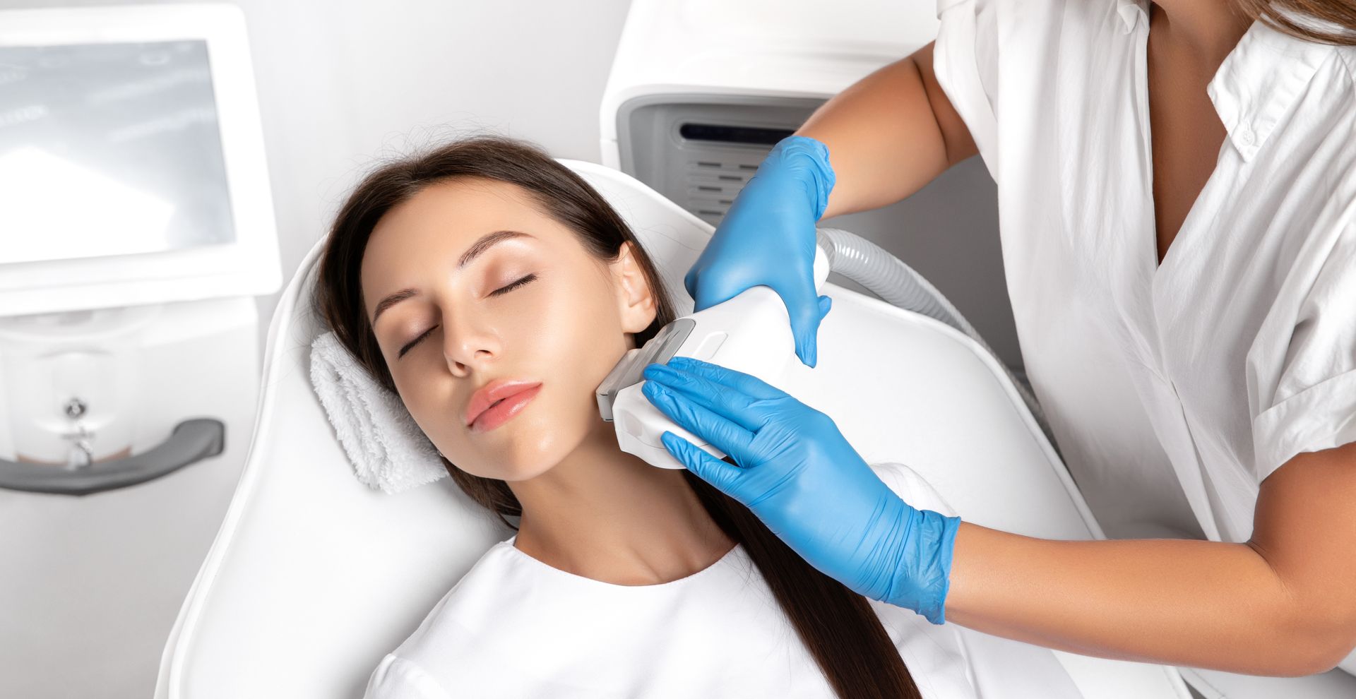 Aesthetic facial treatment on a reclining client, with a practitioner wearing blue gloves.