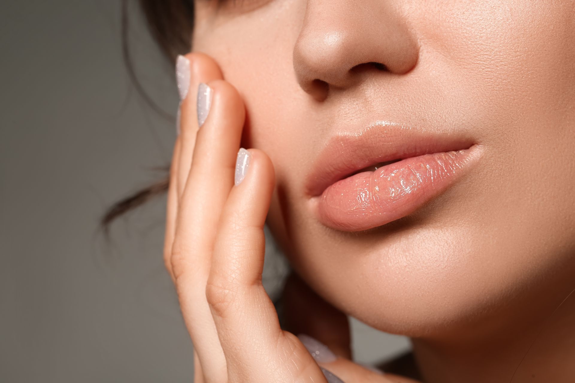 Close-up of a hand touching a woman's cheek and lips, with soft neutral lighting.