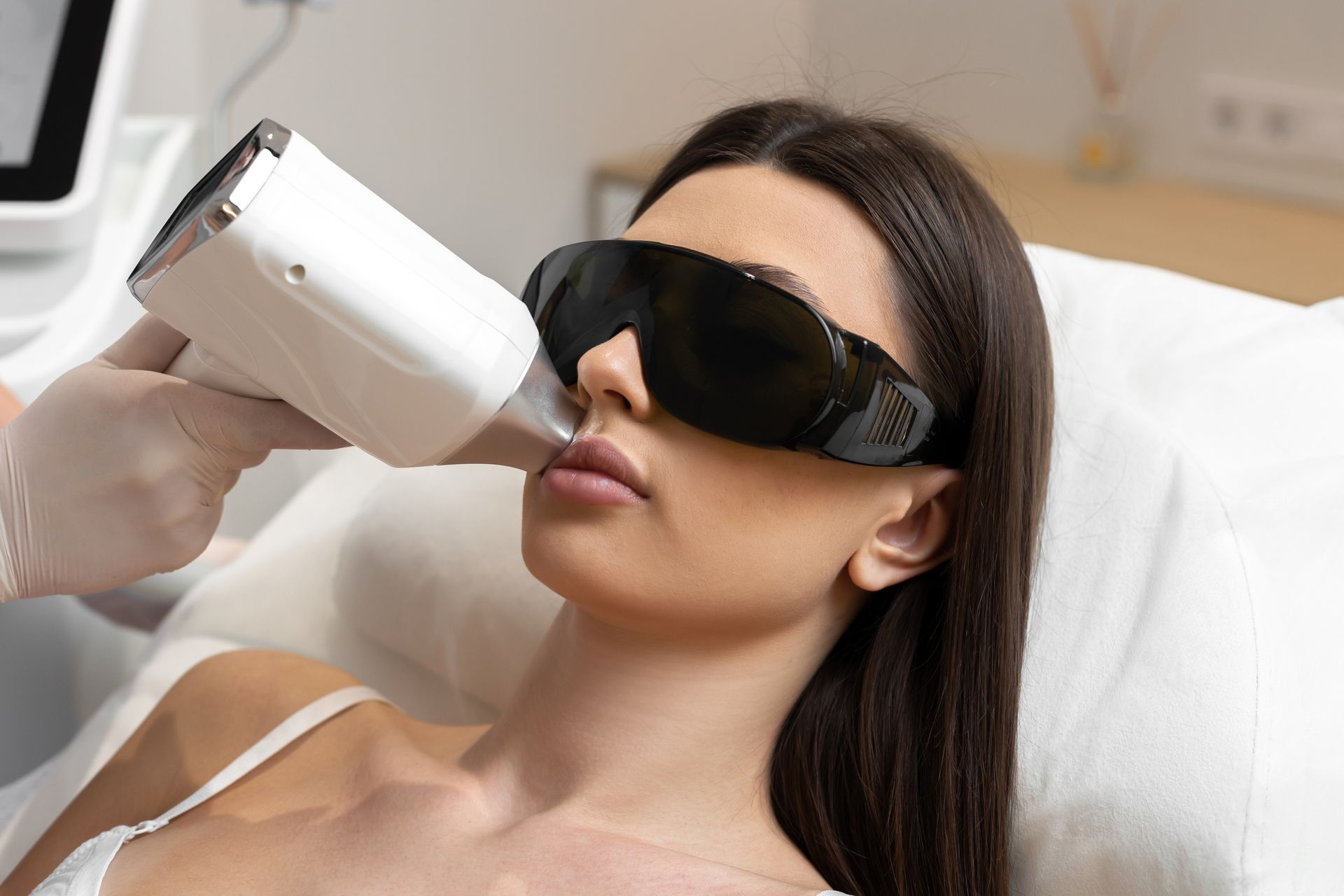 Woman wearing dark goggles receives laser treatment on her face in a clinic setting