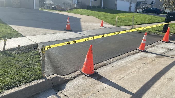 A concrete driveway with orange cones and a yellow caution tape.