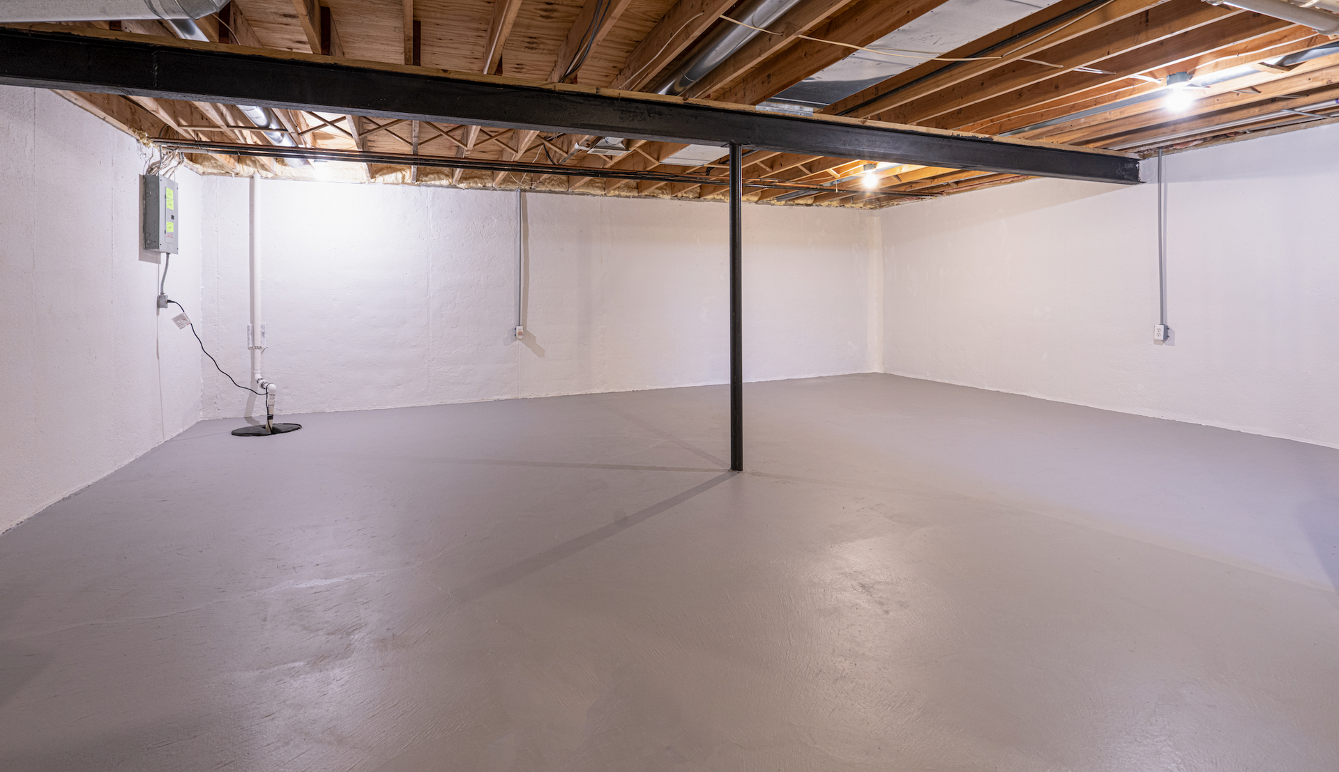 An empty basement with a concrete floor and wooden beams.