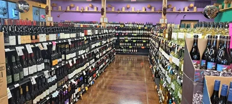 Wine shop aisle with shelves of bottles and a curved wooden floor under purple walls