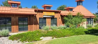 Low wooden building with orange roofs and greenery in front under a blue sky
