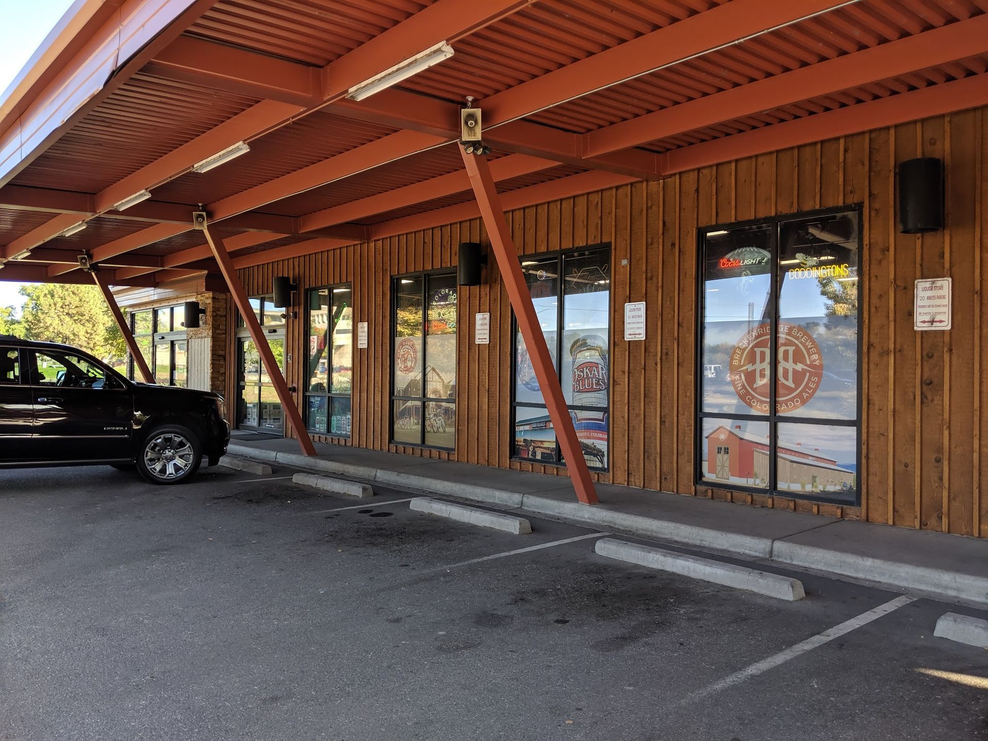 Covered parking area outside a wooden storefront with a black car parked under the roof.