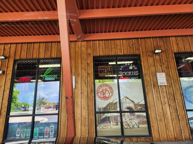 Storefront with wooden siding, glass doors, and neon open signs under a red awning.
