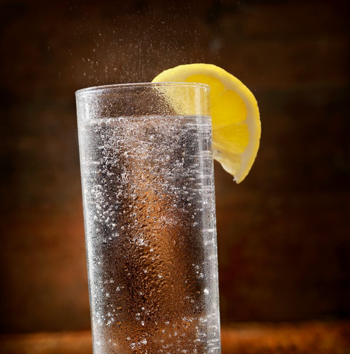 A sparkling clear drink in a tall glass with a lemon slice garnish