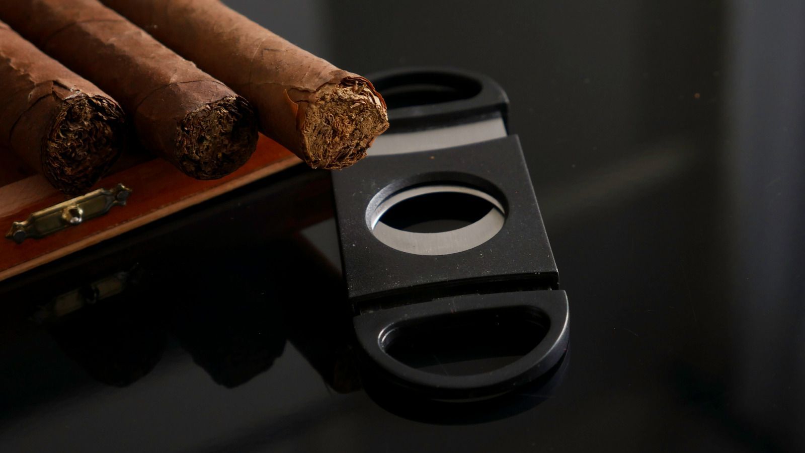 Cigars resting in a black ashtray on a glossy dark table, with a cigar cutter beside them