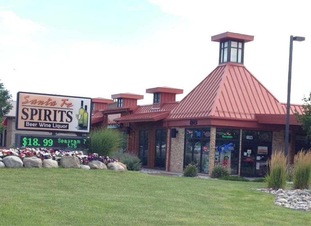 Liquor store with red-roofed entrance and “SPIRITS” sign beside a grassy lawn