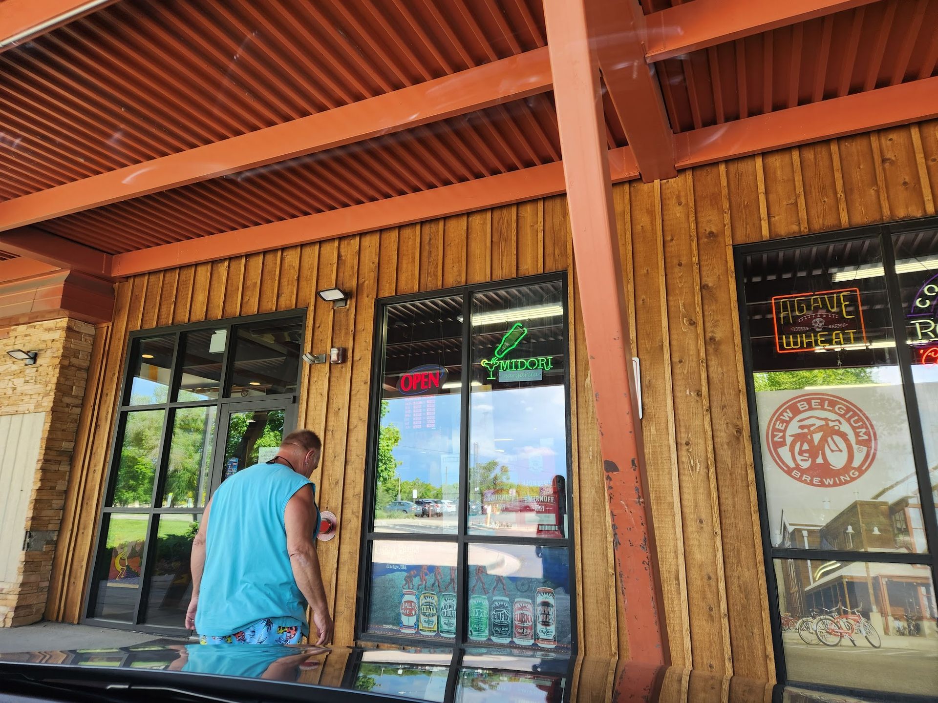 Man in blue shirt opening a wooden door at a storefront with orange awning and glass windows
