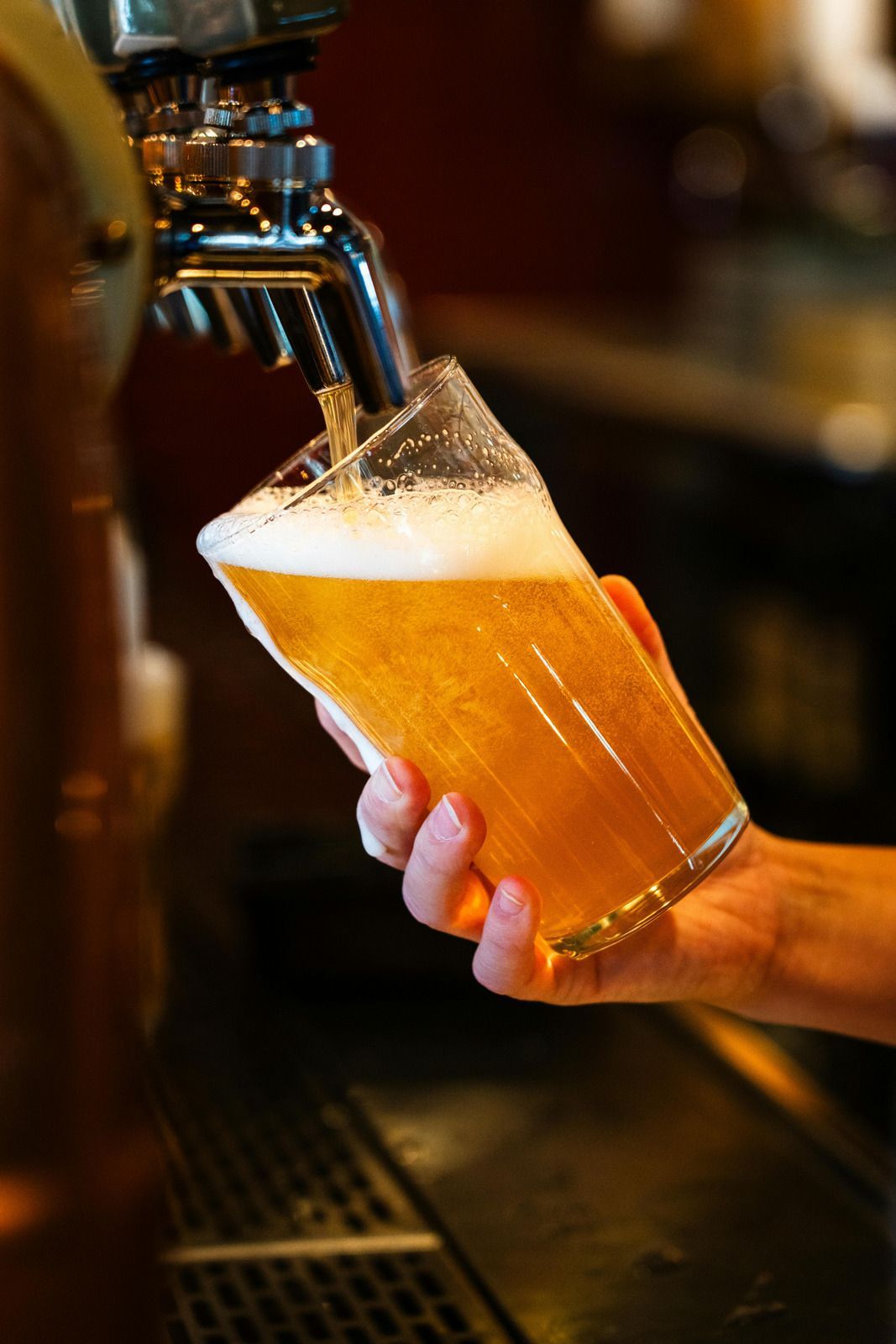 Beer being poured from a tap into a tilted glass, held at a bar.