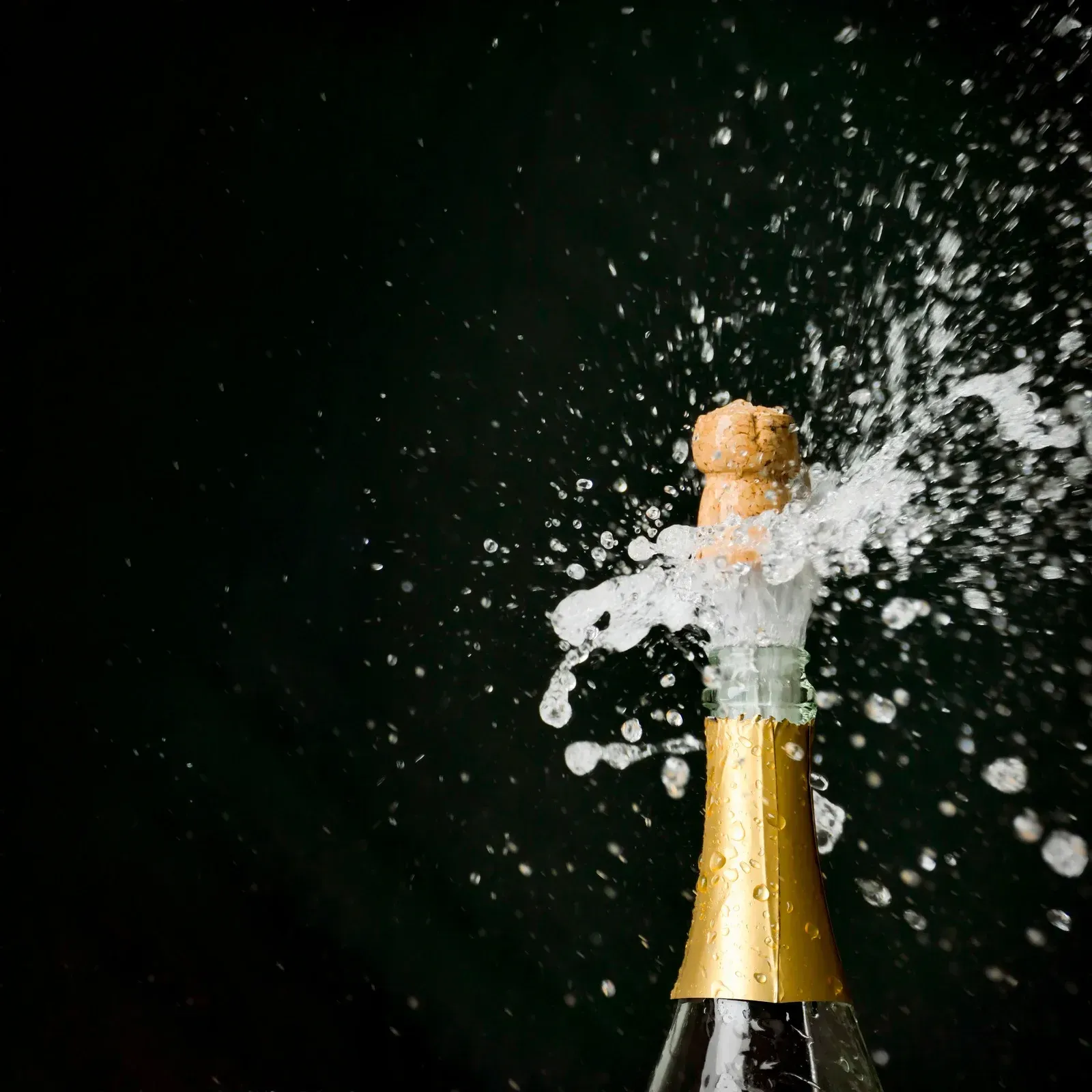 Champagne bottle popping with cork flying and spray bursting against a dark background
