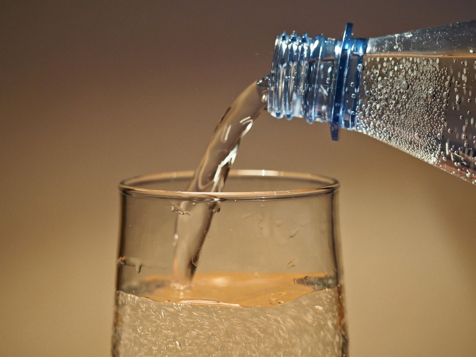 Water pouring from a plastic bottle into a glass on a beige background