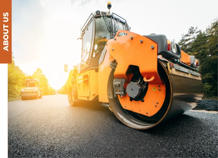 A bright orange steamroller drives on a freshly paved asphalt road during a sunny day.