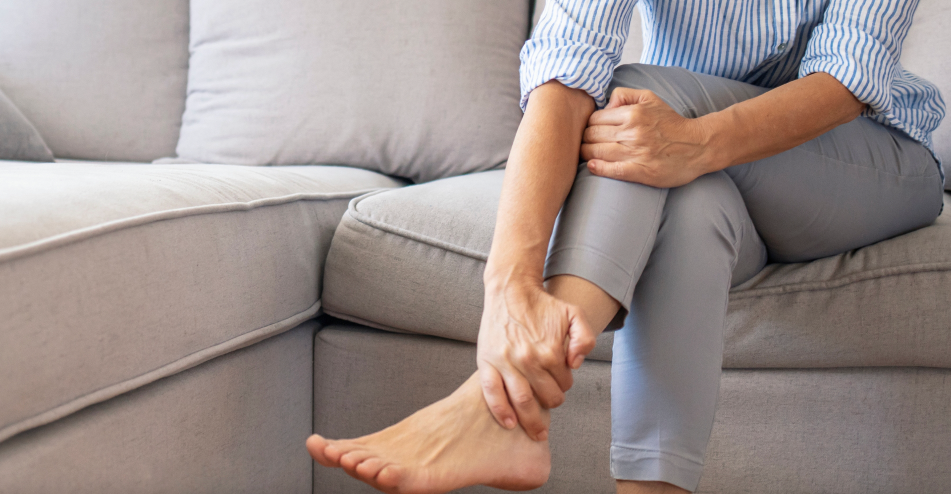 A woman is sitting on a couch holding her foot in pain.