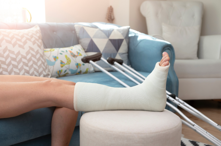 A person with a cast on their leg is sitting on a couch with crutches.