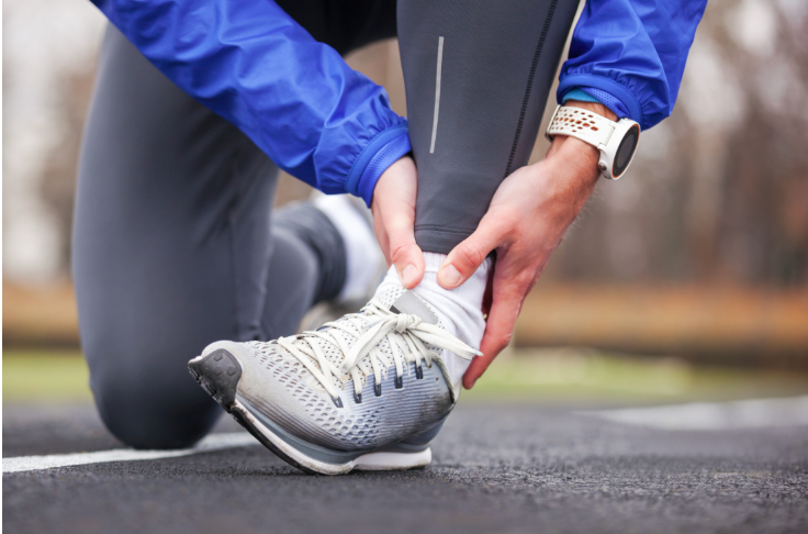 A person is tying their shoes and holding their ankle.