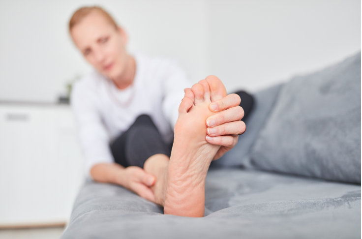 A woman is sitting on a couch holding her foot in pain.