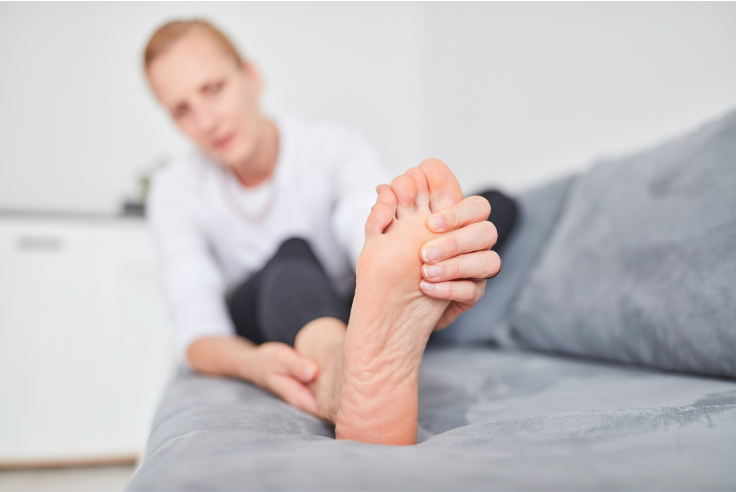 A woman is sitting on a couch holding her foot in pain.