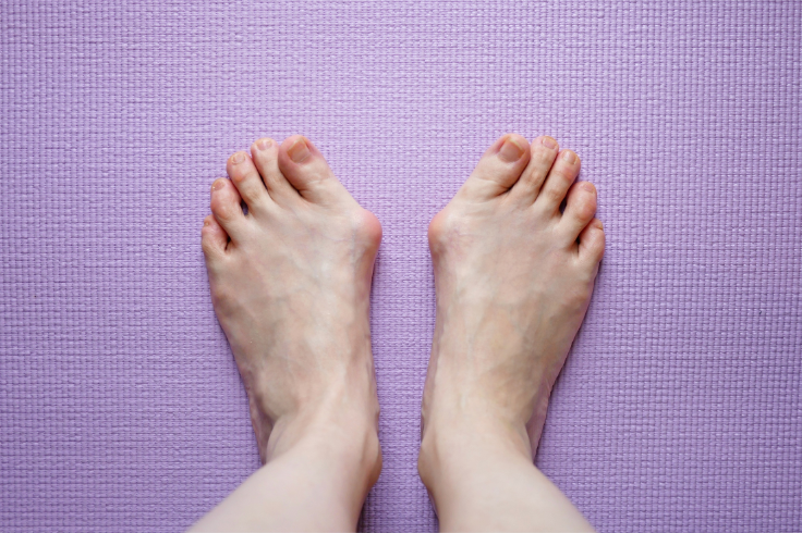 A person 's feet are standing on a purple yoga mat.