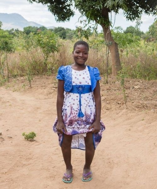 A girl in a blue and white dress is standing in the dirt