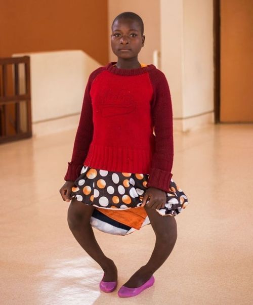 A girl in a red sweater and polka dot skirt is sitting on the floor