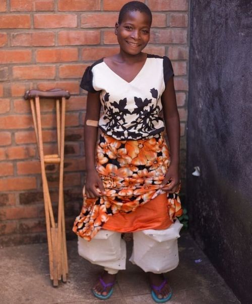 A woman with crutches stands in front of a brick wall