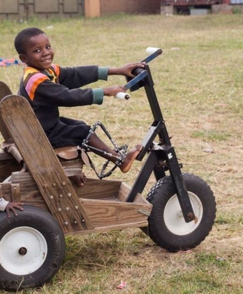 A young boy is riding a wooden tricycle in a field