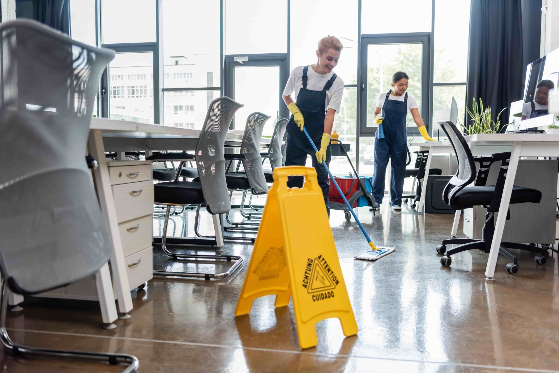 Two people cleaning an office floor with a wet floor sign in front.