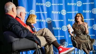 Mesa redonda: Una mujer vestida de leopardo habla con tres personas sentadas frente a un fondo azul de Rotary.
