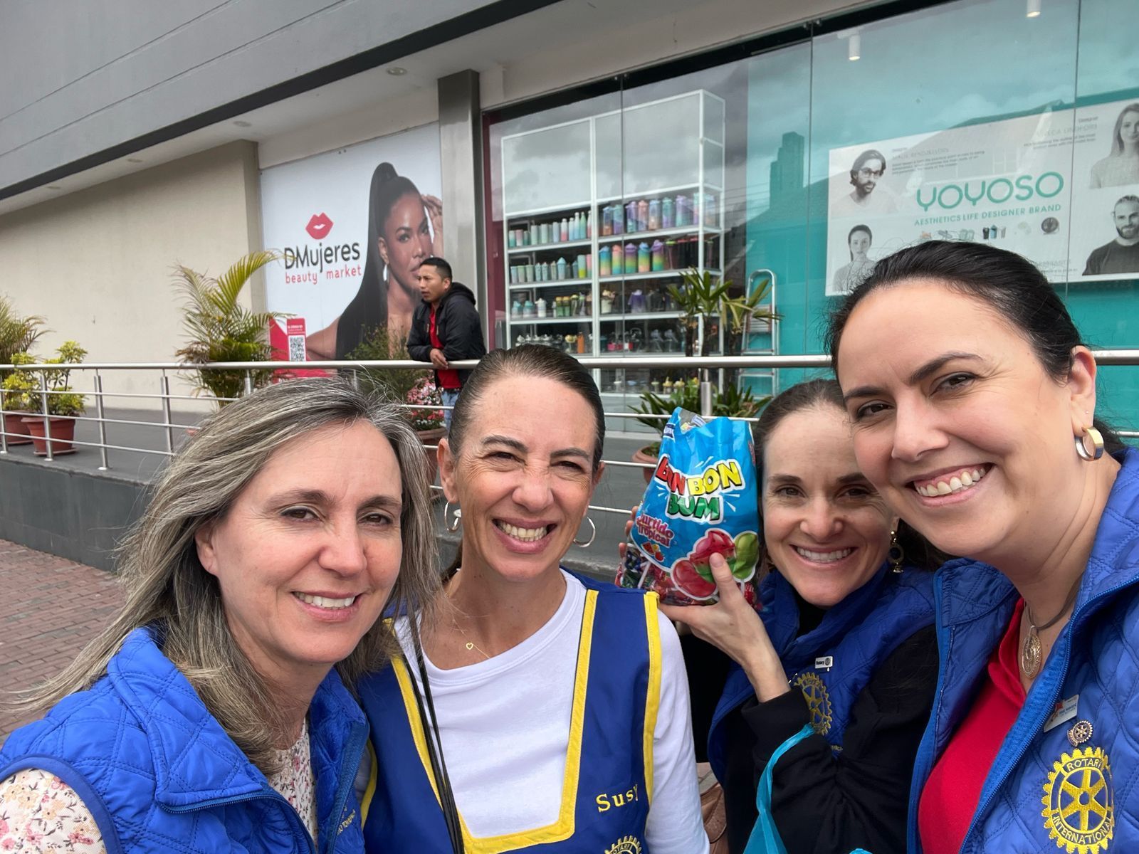 Cuatro mujeres sonriendo al aire libre, con dulces en la mano. Al fondo, una tienda.