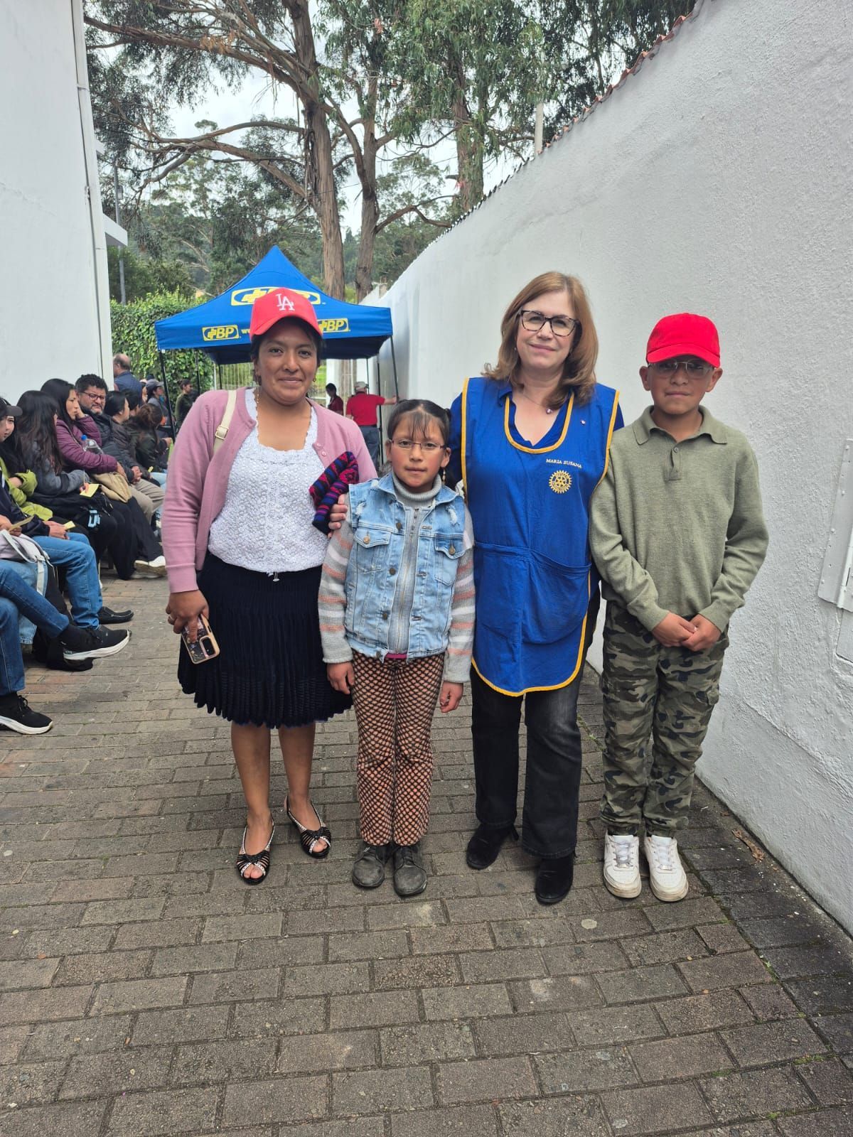 Cuatro personas posando al aire libre: mujer de rosa, dos niños, mujer con chaleco azul.