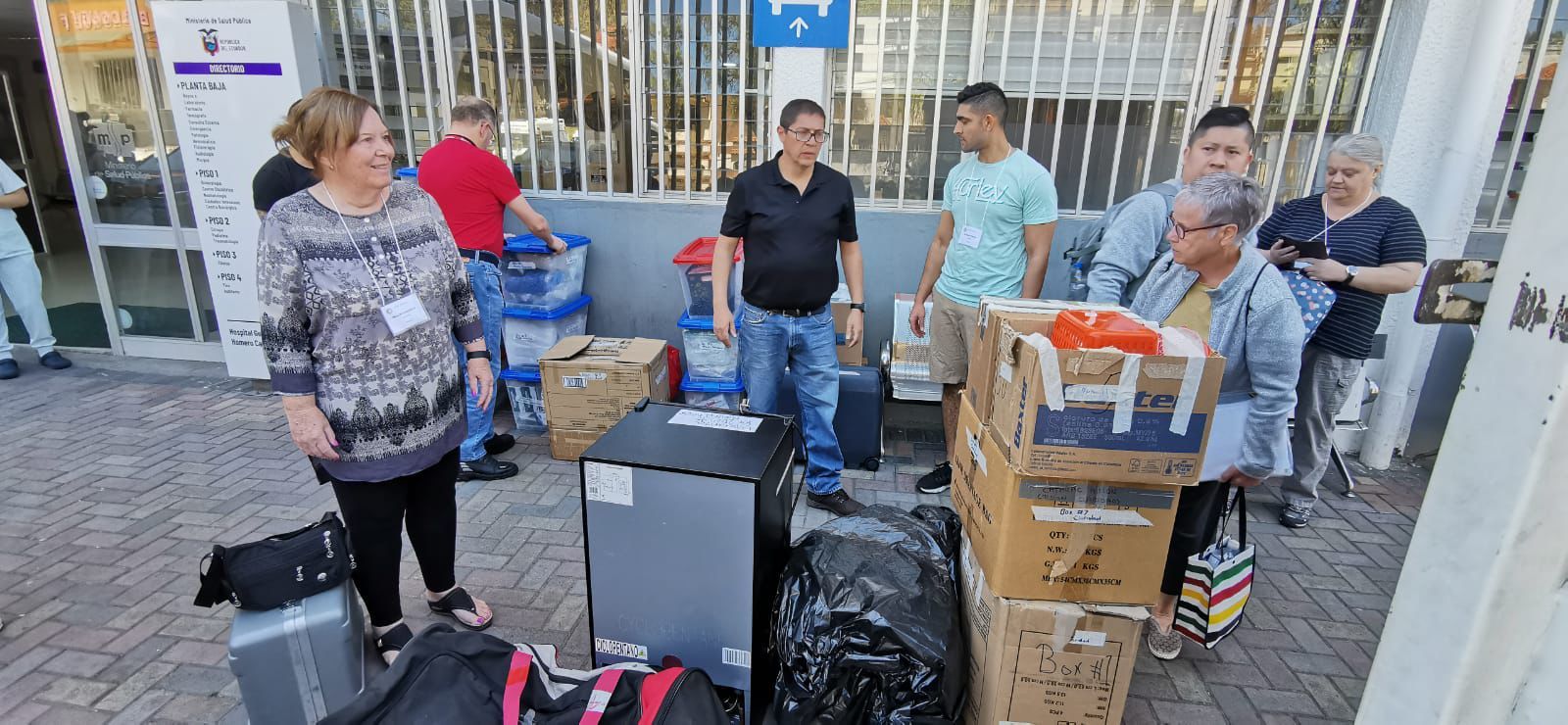 Personas descargando equipaje y cajas afuera de un edificio.