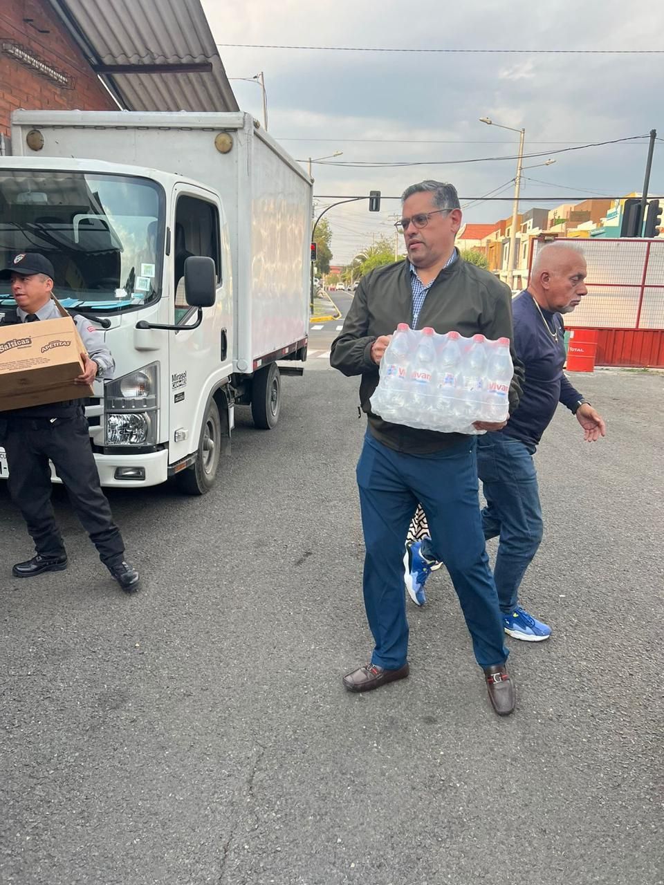 Personas cargando botellas de agua y cajas desde un camión de reparto en una calle.