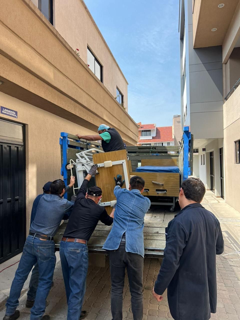 Hombres empujando muebles hacia un camión en un callejón estrecho, un día soleado.