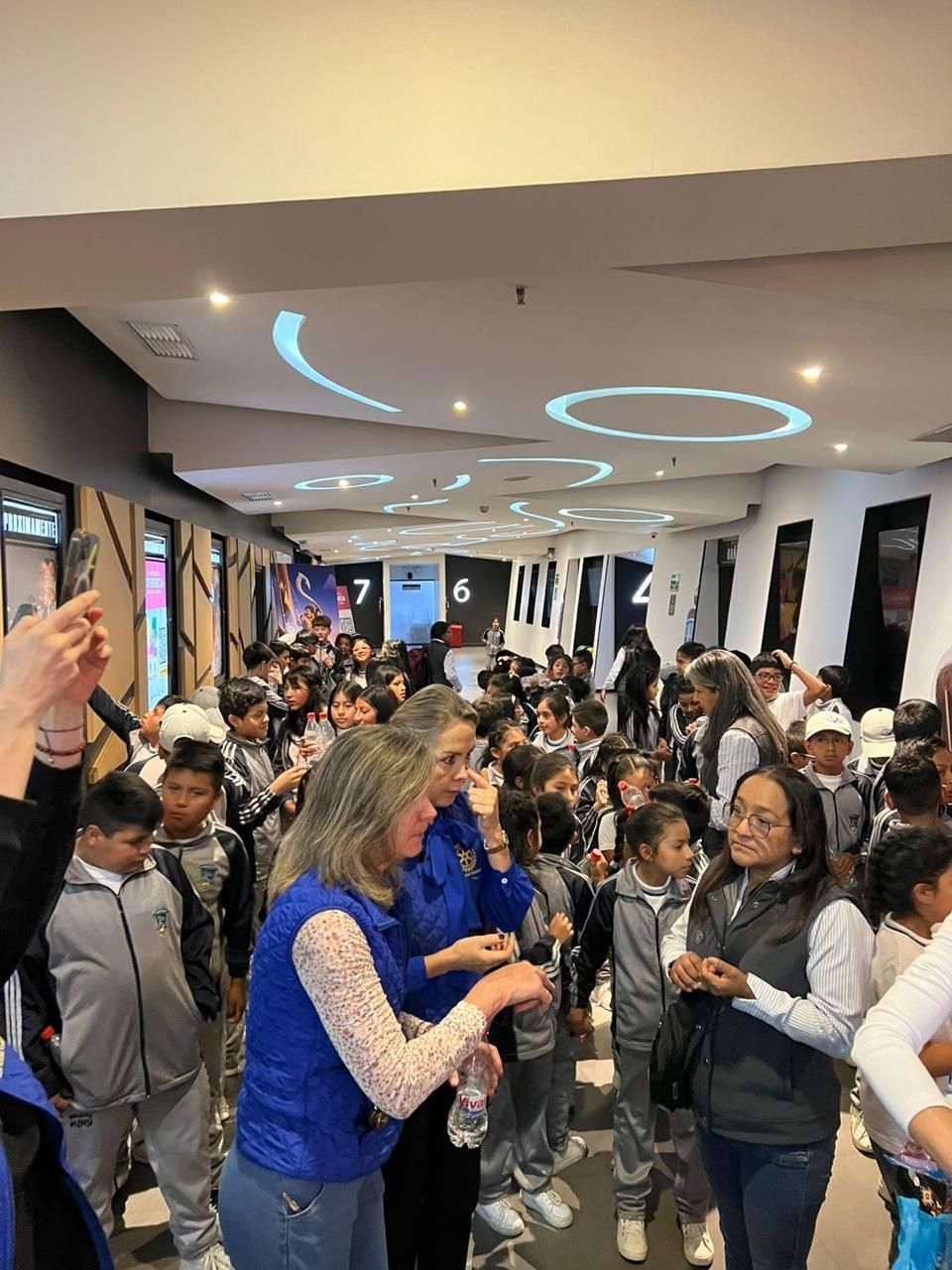 Niños y adultos en un cine. Grupo de estudiantes uniformados, dos mujeres de azul.