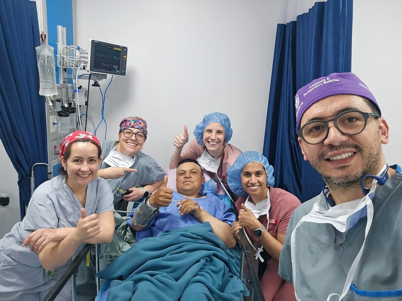 Equipo médico sonriente con un paciente haciendo un gesto de aprobación. Habitación de hospital.