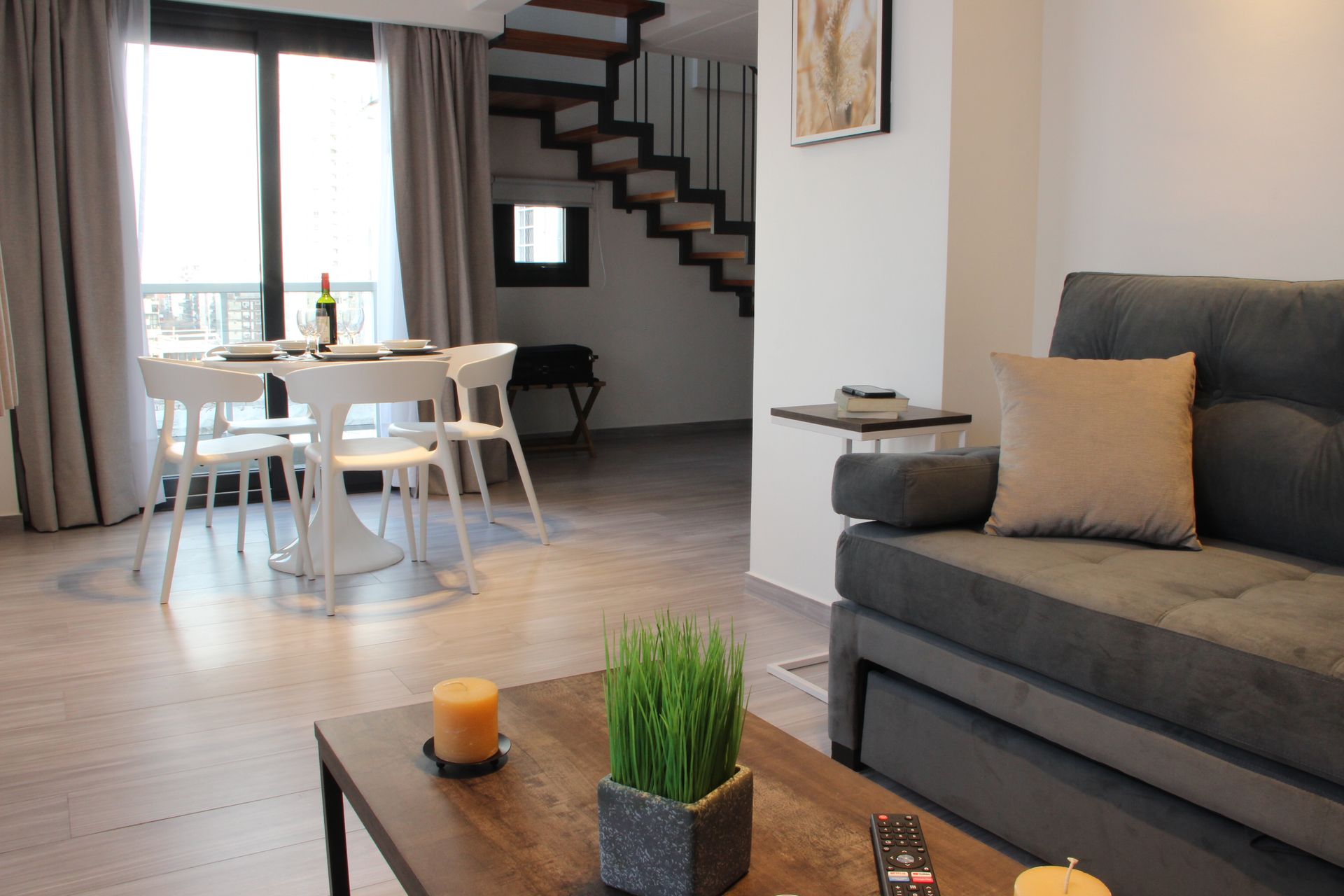 Modern living room with gray sofa, coffee table, dining area, and staircase in the background