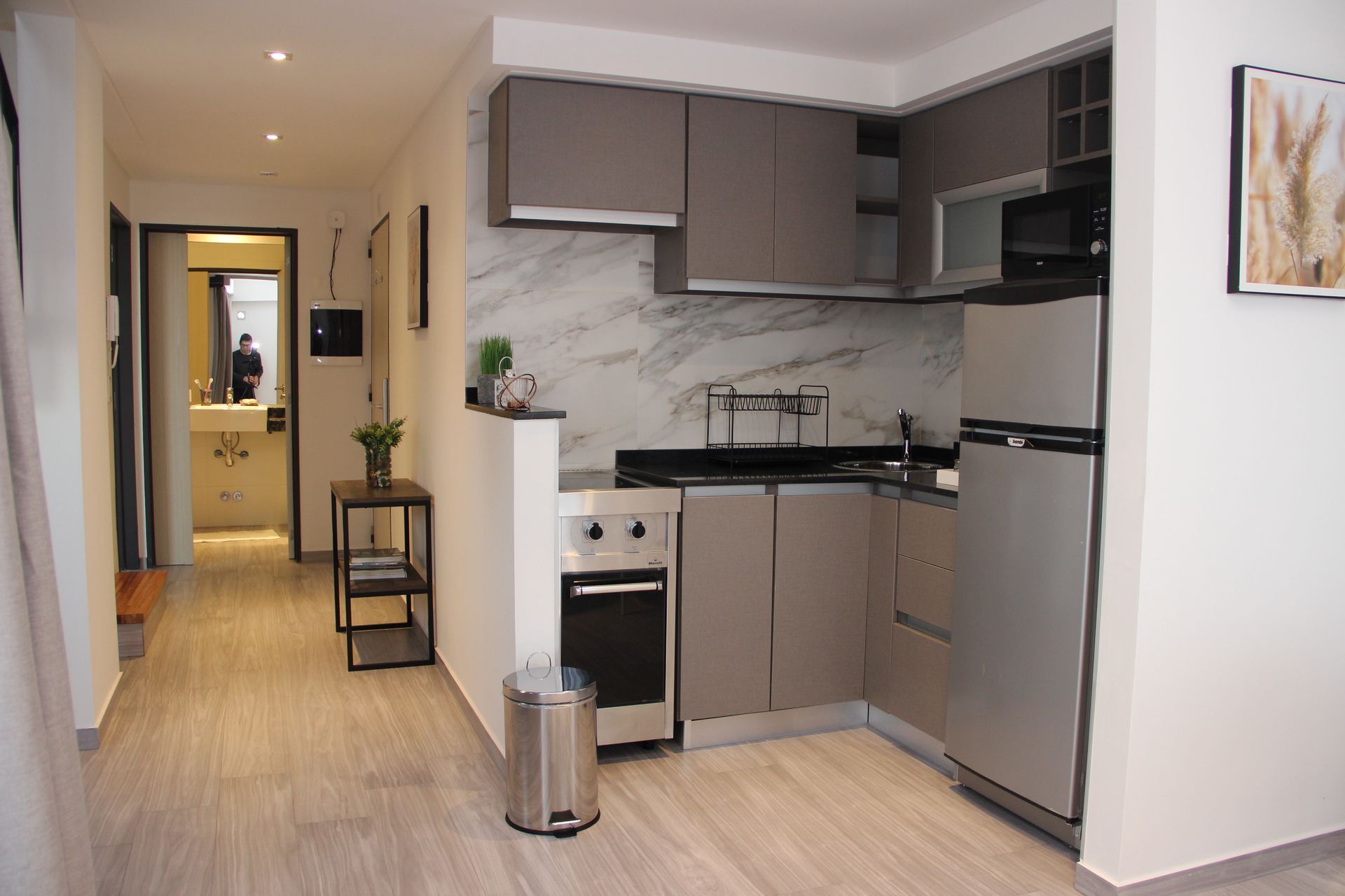 Compact kitchen with gray cabinets, stainless fridge, and a hallway in a modern apartment