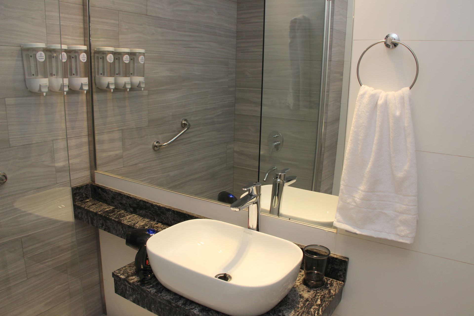 Modern bathroom vanity with white sink, large mirror, glass shower, and a towel ring.