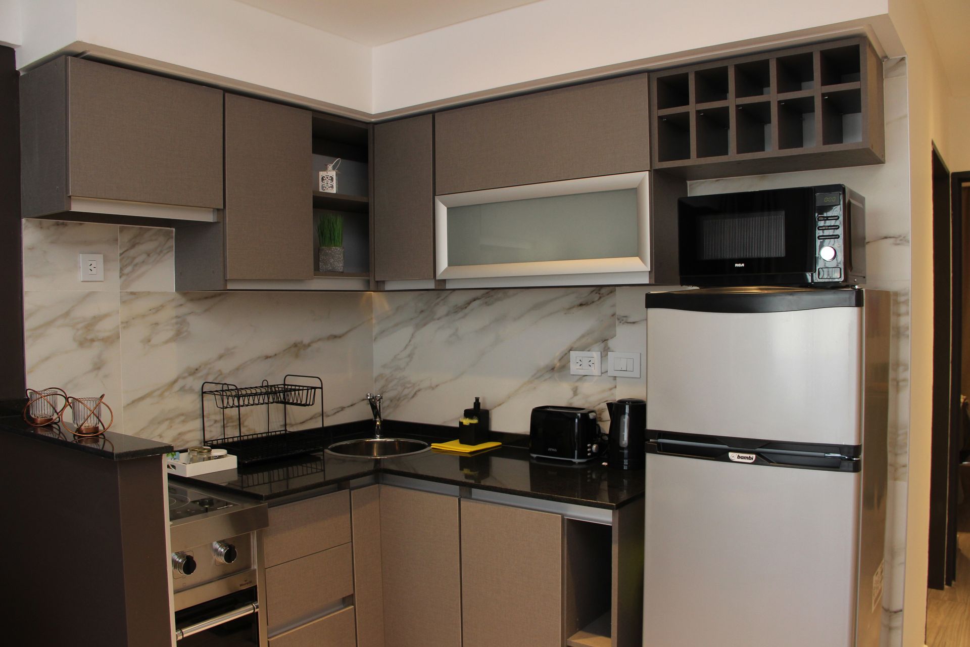 Compact kitchen with gray cabinets, black countertops, white tile backsplash, and a refrigerator with microwave.